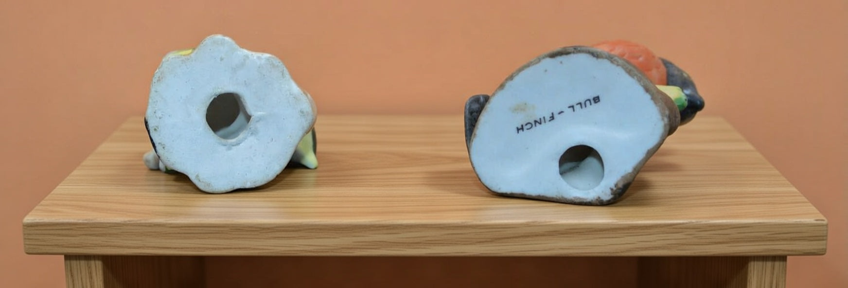 Underside of two vintage ceramic bird figurines showing base holes and printed “Bullfinch” marking, glazed white bases with age-related wear, collectible bird ornament detail view