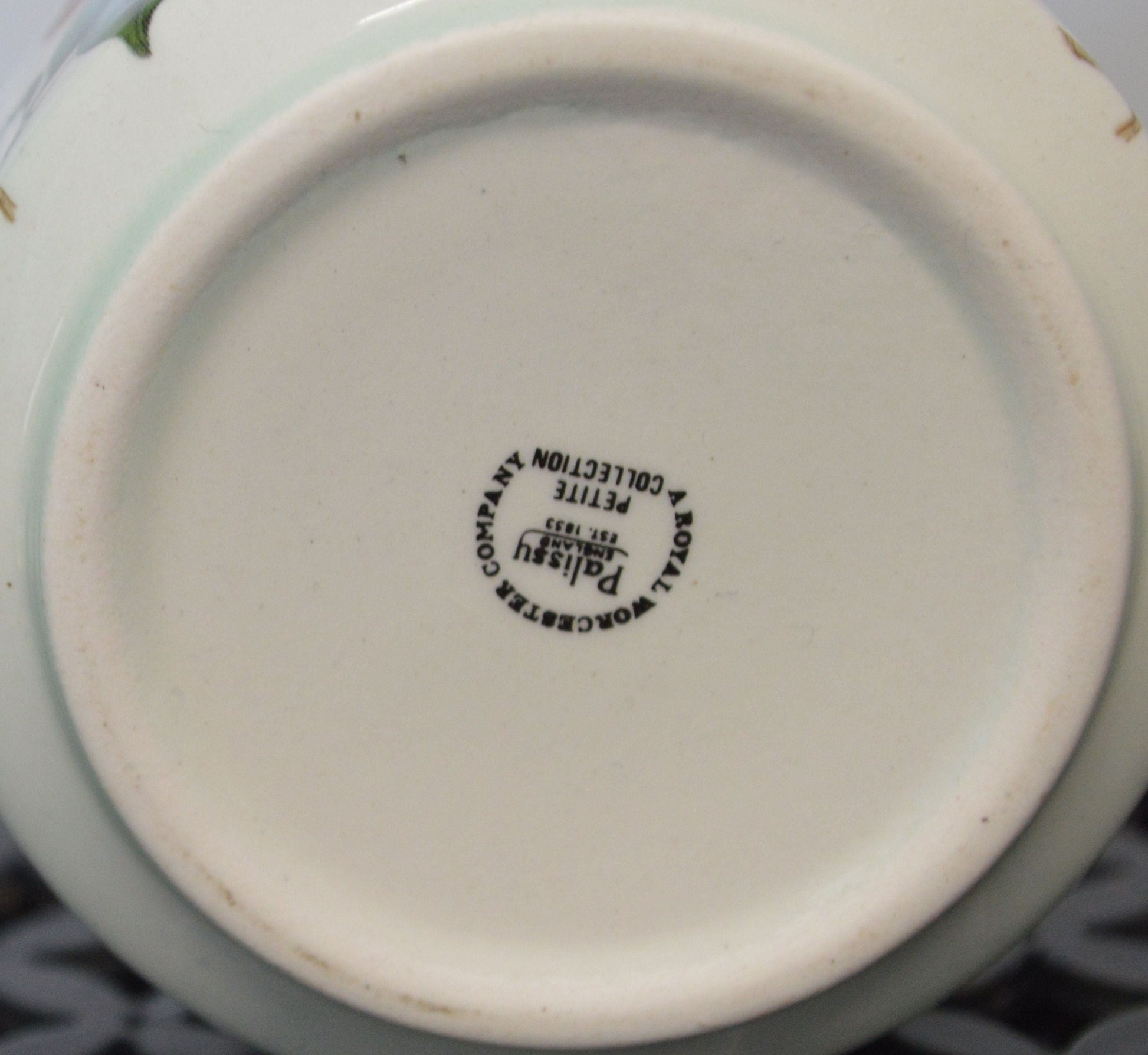 The bottom of the ceramic box is shown, displaying the manufacturer's mark in black text. The text reads, "Palissy, England, Est. 1853, Petite, A Royal Worcester Collection" in a circular format, indicating it is part of a royal porcelain collection.
