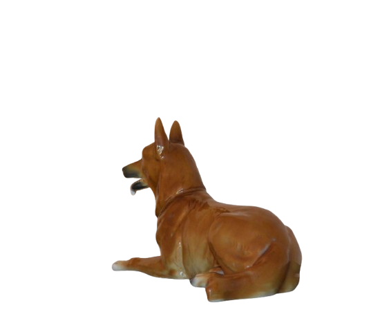 Ceramic dog figurine viewed from the side and back, showing perked ears, open mouth, and a glossy brown finish. The dog is lying down with its back legs tucked under."