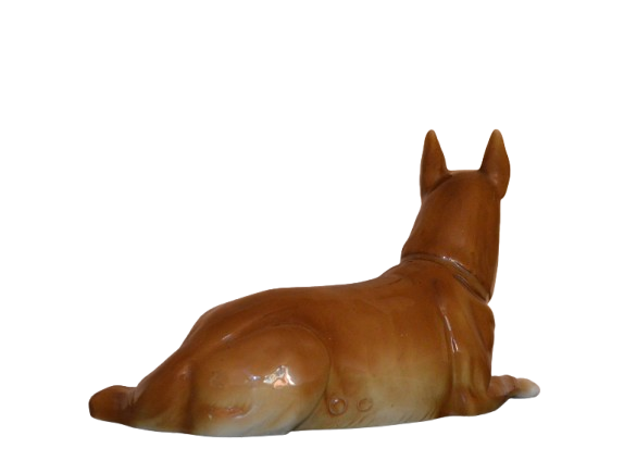 Back view of a ceramic dog figurine with perked ears and a glossy brown finish. The dog is lying down with its hind legs stretched out and tail resting on the ground."