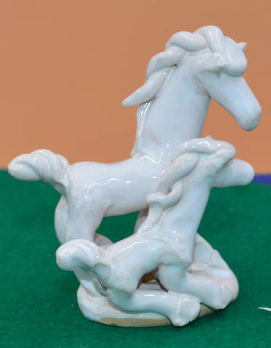 Side view of a white ceramic figurine featuring an abstract adult horse standing beside a foal