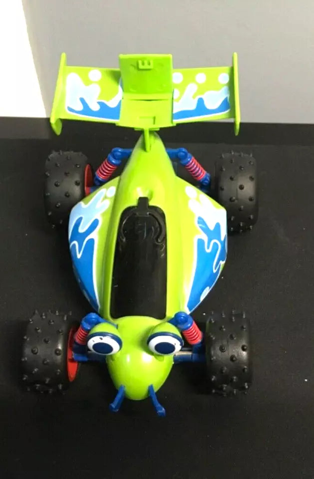 Top view of the Toy Story RC car, featuring a green and blue color scheme with white detailing and expressive eyes on the front. The car has four black wheels with red suspension springs and a large rear spoiler. The interior seating area is visible, showing signs of play wear."