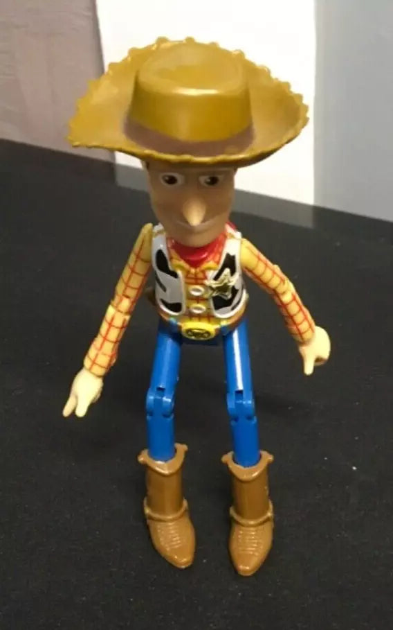 Toy Story Woody action figure standing upright, wearing his signature cowboy hat, red bandana, checkered shirt, blue jeans, and brown boots. The figure has jointed legs and arms for posing and shows signs of play wear."