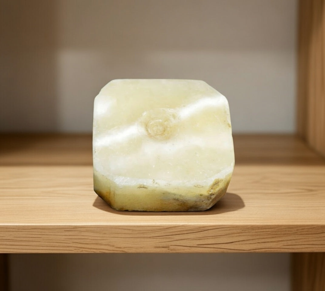 Underside of white marble base from stone swan figurine showing natural stone pattern and wear, decorative rock ornament base detail on wooden shelf.