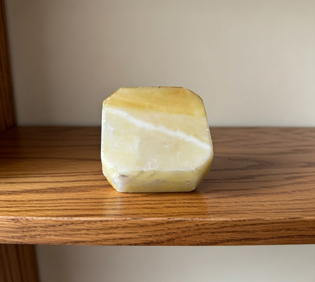 Side view of white marble base used for stone swan figurine, natural stone with cream and yellow veining displayed on wooden shelf.