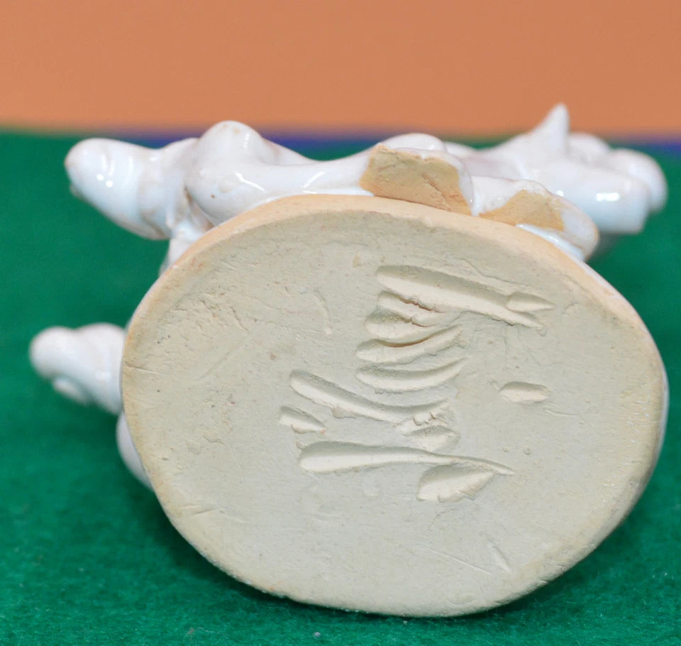 Underside of a white ceramic horse figurine showing an unglazed oval base with an incised maker's mark or signature in an unknown script